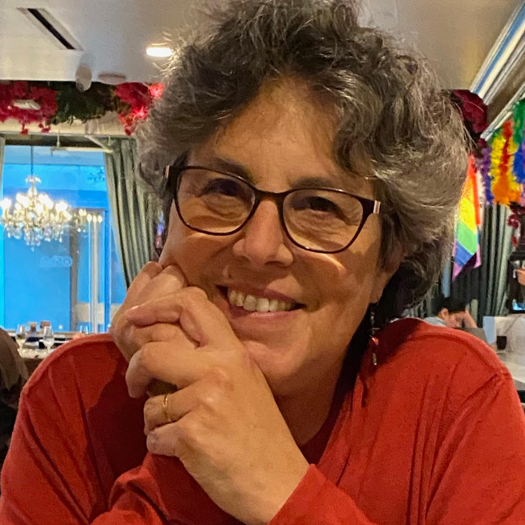 casual photo of jenny walter in a red shirt with her hands by her face. she has short wavy gray-brown hair, glasses