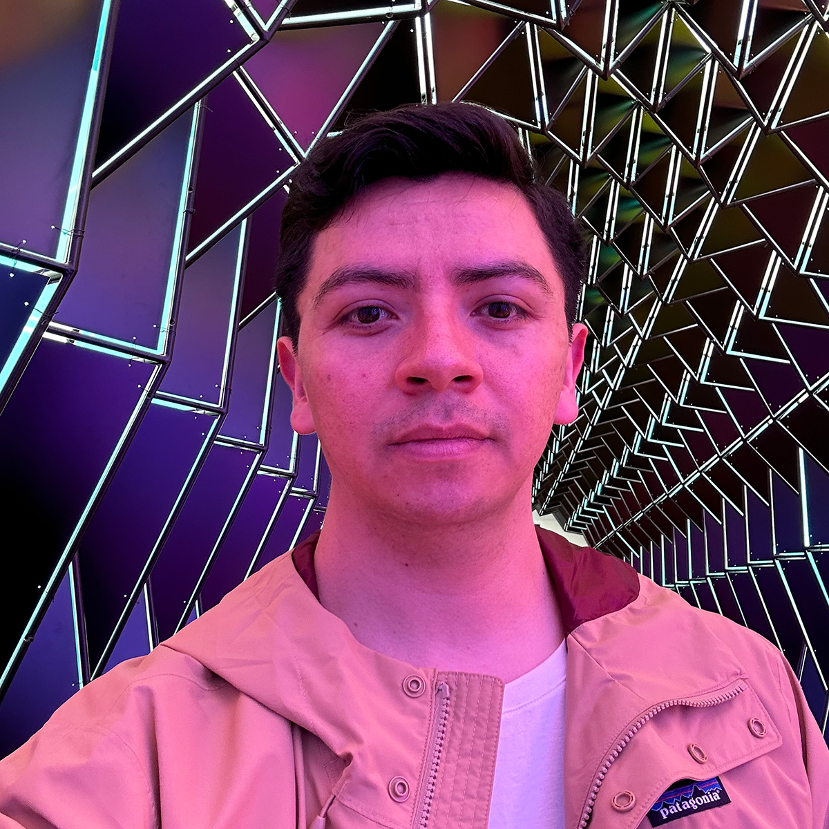 rodolfo reyes is a young person with short brown hair, wearing a beige patagonia jacket in front of an ai-generated kaleidoscopic image
